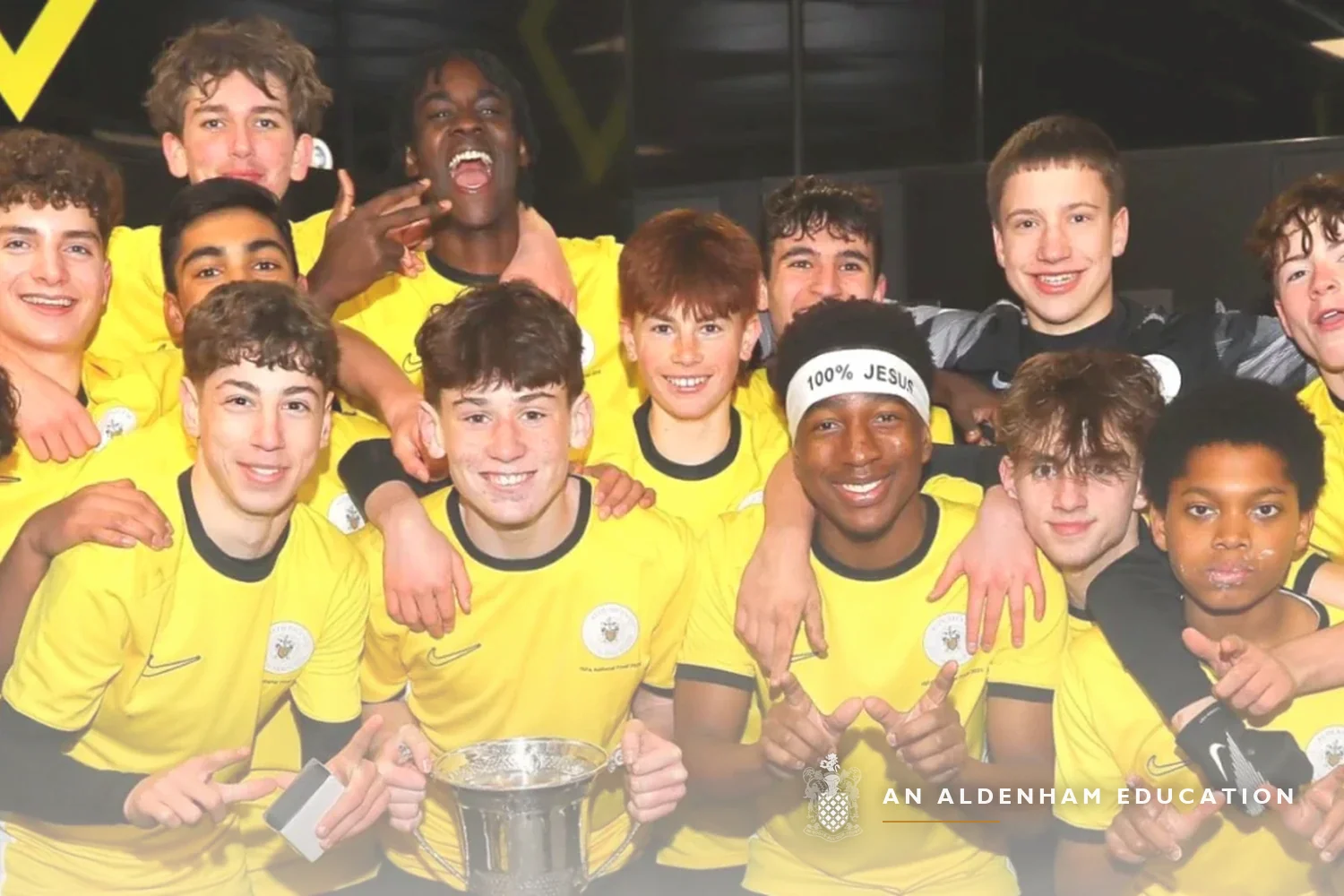 An Aldenham football squad in yellow kit celebrating together with a trophy after a match